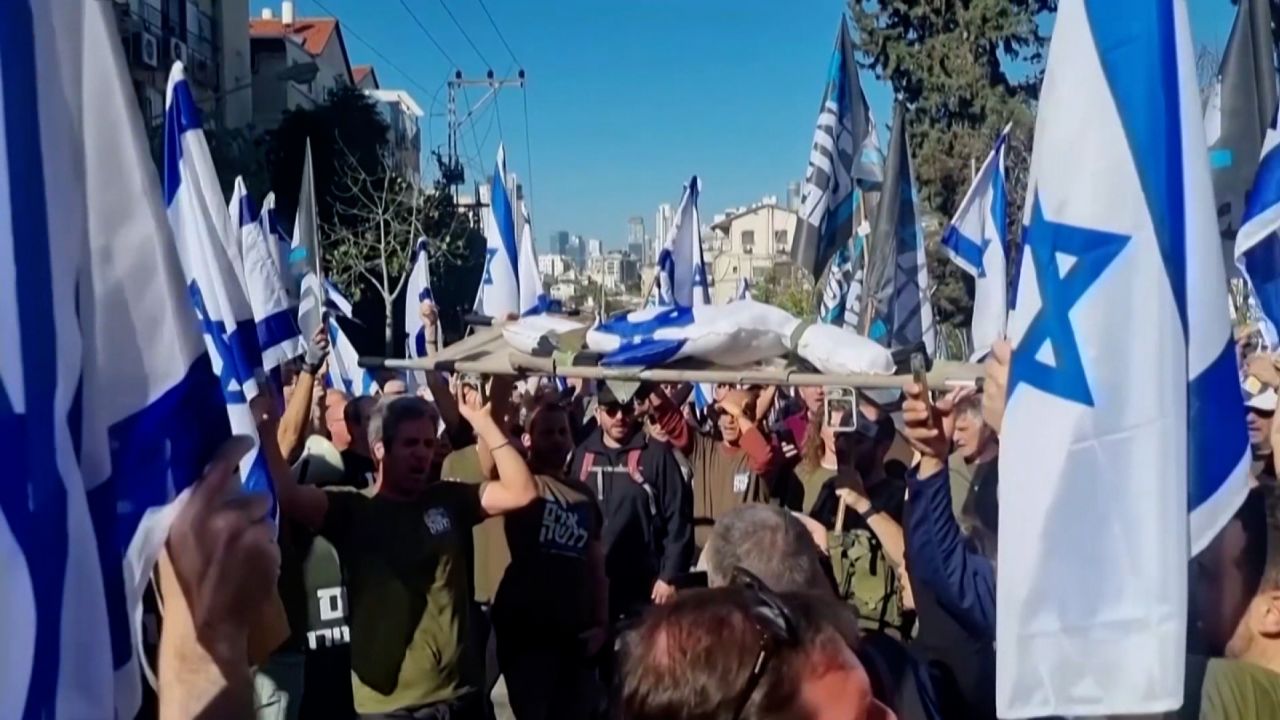 Silah Arkadaşları'ndan bir grup, İsrail bayrağına sarılı bir figürü, yaralı bir yoldaşı saha dışına taşır gibi sedye üzerinde taşıyarak protesto ediyor.