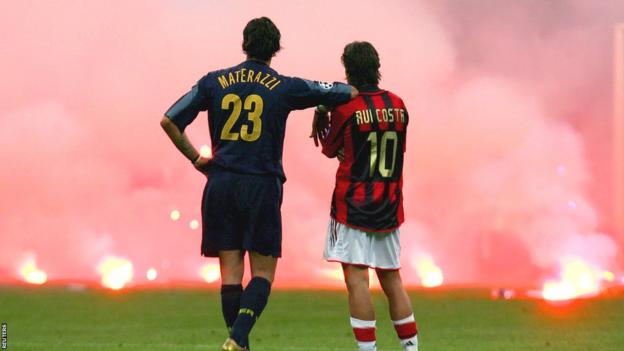 Marco Materazzi, AC Milan ile Inter Milan arasında oynanan 2005 Şampiyonlar Ligi çeyrek finali sırasında tribünlerden atılan işaret fişeklerinden yükselen dumanı izlerken Rui Costa'nın omzuna yaslanmış durumda.